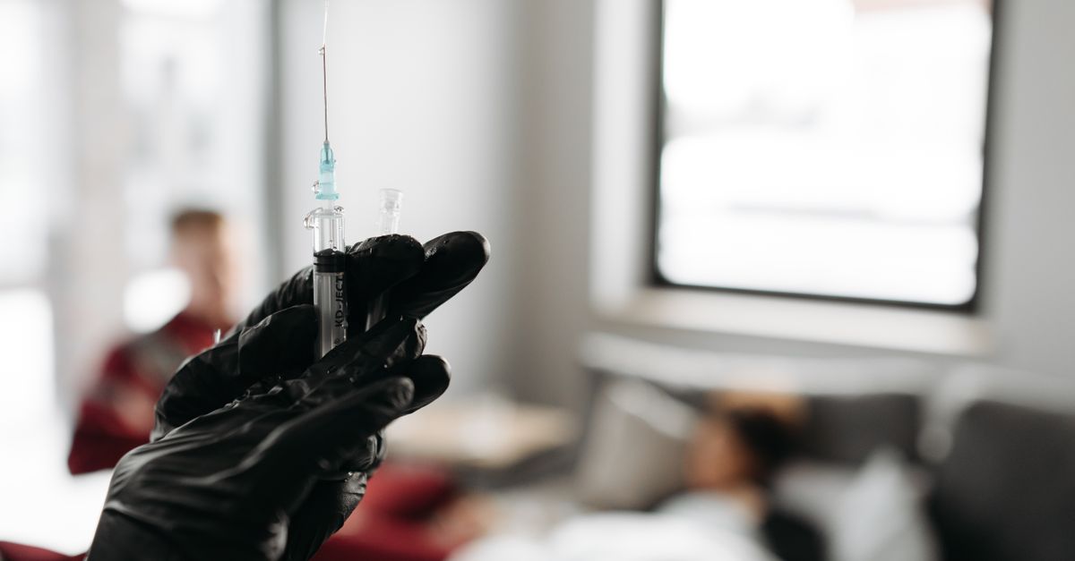 Close-up of a gloved hand holding a syringe in a medical setting with blurred background.